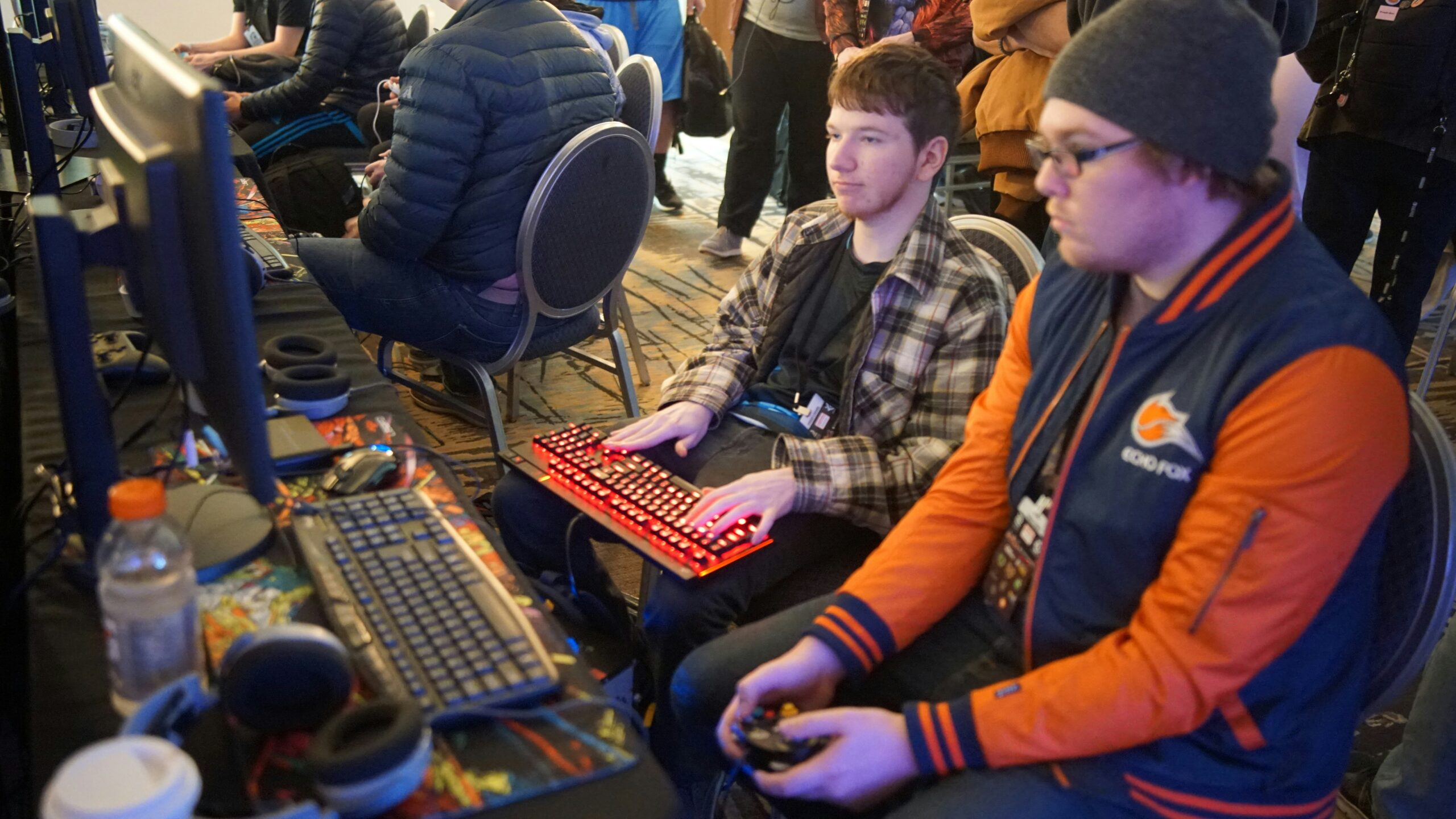 Group of gamers with headsets playing MMORPG - man using video game control pad beside man using computer keyboard sitting and playing video games